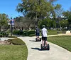 Three people are posing with Segways on a residential street wearing helmets and smiling with the signage indicating they are part of a tour group