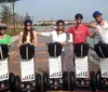 Three people are posing with Segways on a residential street wearing helmets and smiling with the signage indicating they are part of a tour group