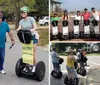 Three people are posing with Segways on a residential street wearing helmets and smiling with the signage indicating they are part of a tour group