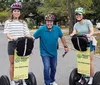 Three people are posing with Segways on a residential street wearing helmets and smiling with the signage indicating they are part of a tour group