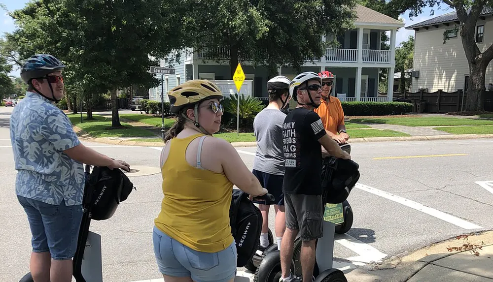 A group of people wearing helmets are preparing for or taking a break from riding Segways on a sunny day on an urban street
