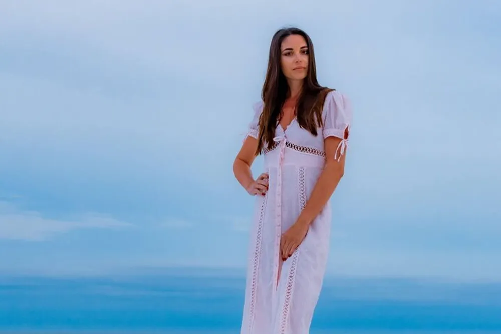A woman in a white dress stands against a serene blue backdrop that may be the sky or the sea
