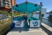 The image shows a turquoise-covered cycle boat docked at a pier, adorned with marine-themed decorations, ready for a leisurely excursion on the water.