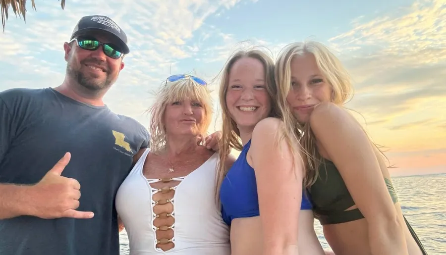 A group of four people are posing happily for a photo by the ocean during sunset.