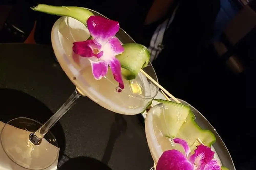 Two elegant cocktails garnished with orchids and slices of cucumber are presented on a dark surface creating a sophisticated and visually pleasing aesthetic