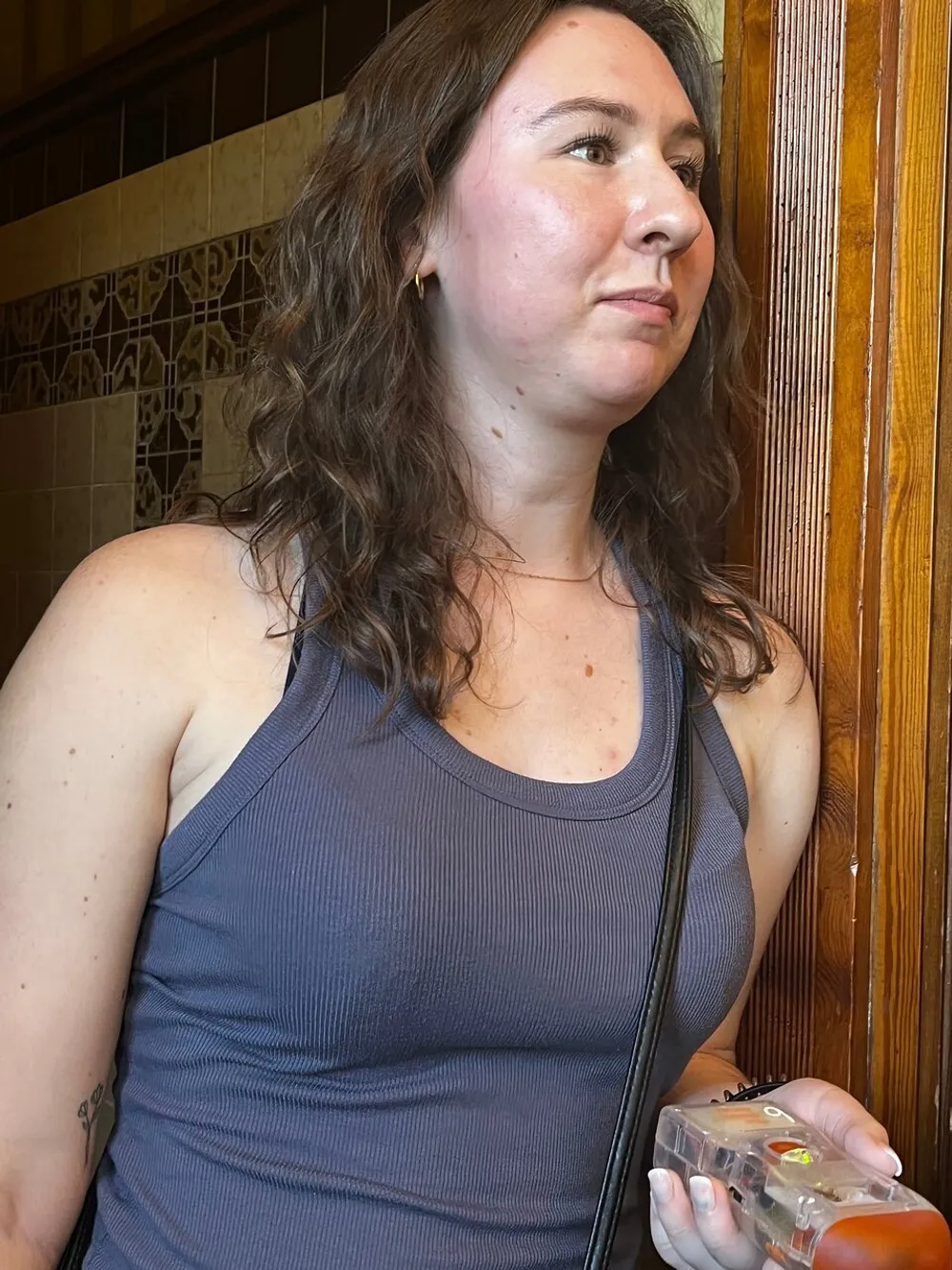 A woman with brown hair wearing a sleeveless top is holding a plastic container likely with some food items inside as she looks off to the side with a contemplative or distracted expression