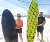 A man and woman are smiling and posing with surfboards on a sunny beach