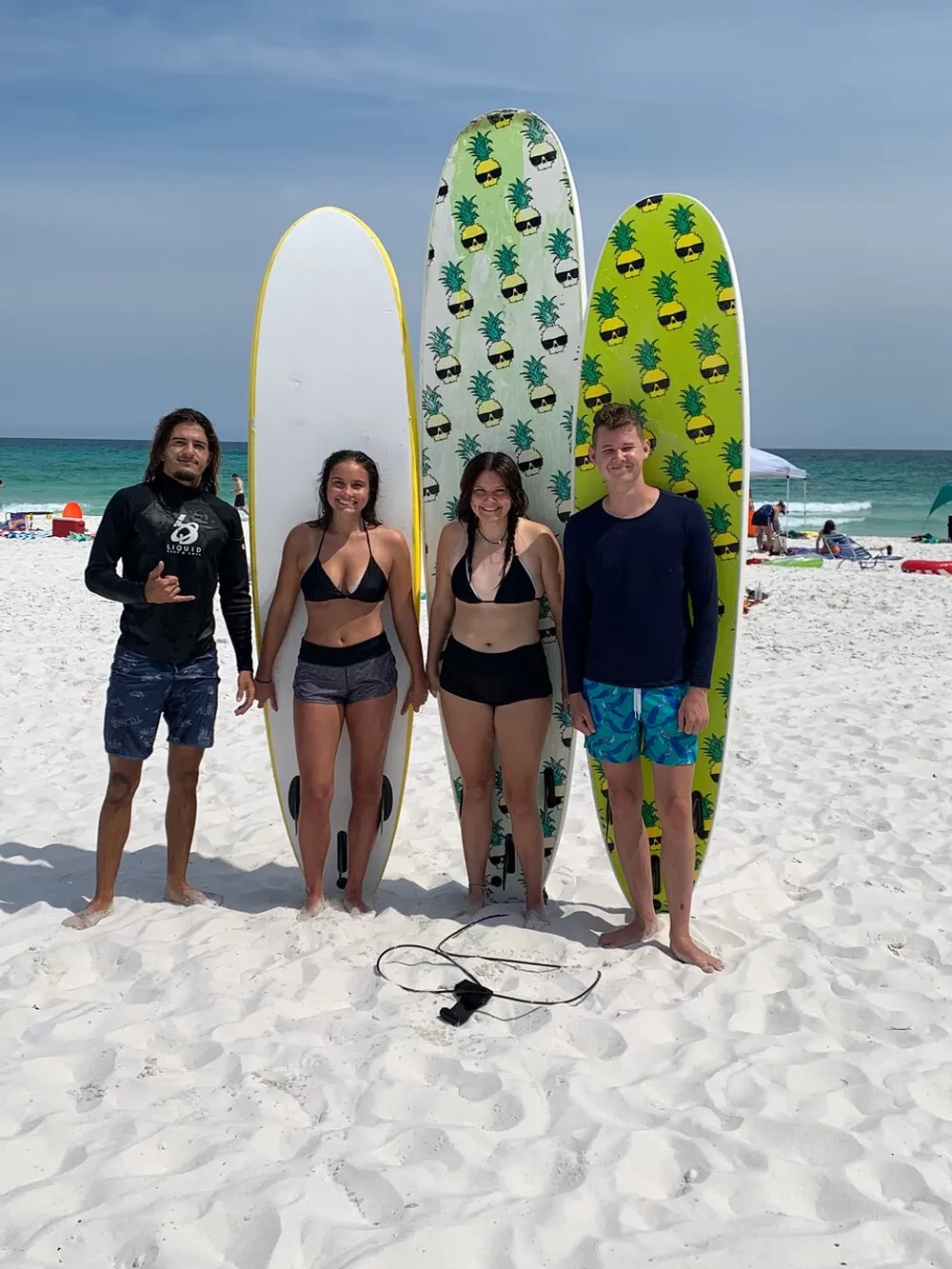 Four people are standing on a sandy beach holding surfboards with the ocean in the background
