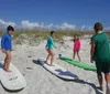 Five individuals are standing on a sunny beach with surfboards smiling and ready for water activities