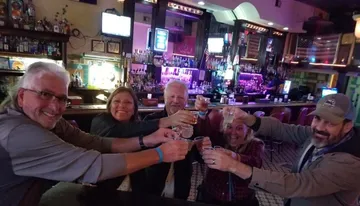 A group of five cheerful people are toasting with shot glasses at a bar with a festive atmosphere.