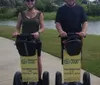 Three people are smiling for the camera with two women standing on Segways and a man standing between them on a road all wearing safety helmets