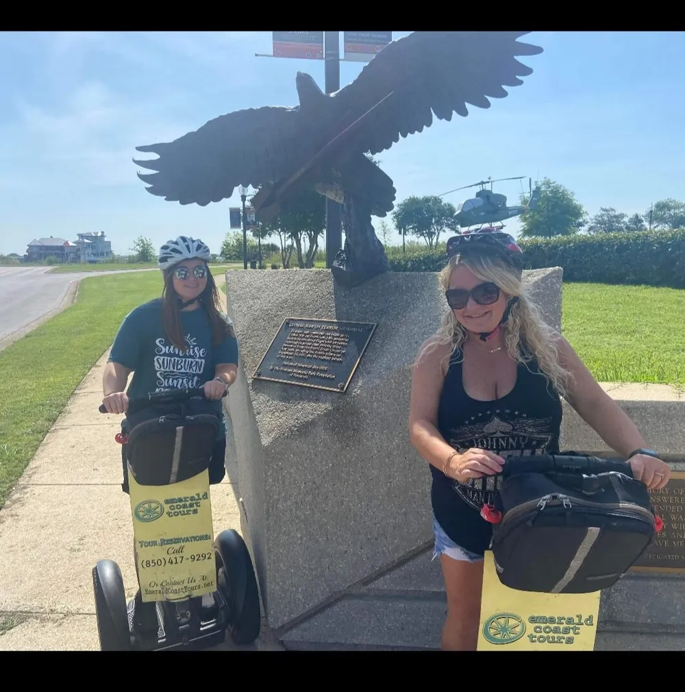 Two people on a Segway tour pose with smiles beside a sculpture of an eagle with a clear blue sky in the background