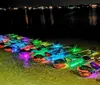 Four people including a child are enjoying a night paddle in a transparent kayak illuminated with colorful lights under the boat
