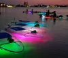Four people including a child are enjoying a night paddle in a transparent kayak illuminated with colorful lights under the boat