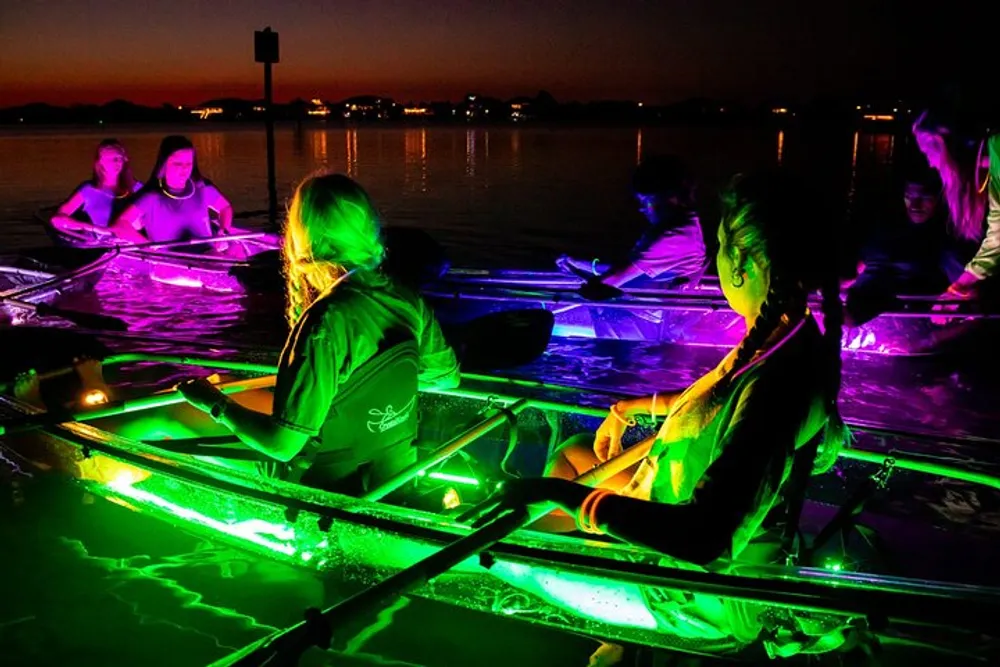 A group of people are kayaking at night with their kayaks illuminated by vibrant green lights under a dusky sky