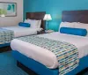 This image shows a brightly colored double bedroom with two beds complementary bold blue and white decor and a modern abstract painting adorning the wall