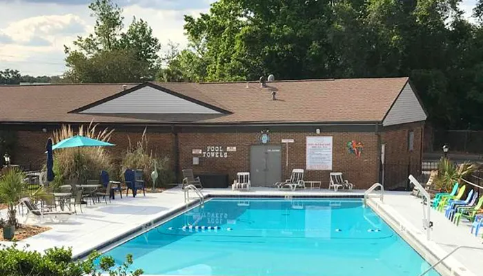 This image shows a serene outdoor swimming pool area with chairs around a towel service hut a blue umbrella and a sign indicating pool safety rules