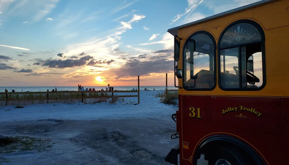 A trolley is parked near a beach where people are enjoying a picturesque sunset