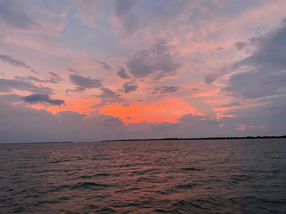 The image captures a serene sunset with vibrant shades of pink and orange spreading across a cloud-streaked sky over a calm body of water