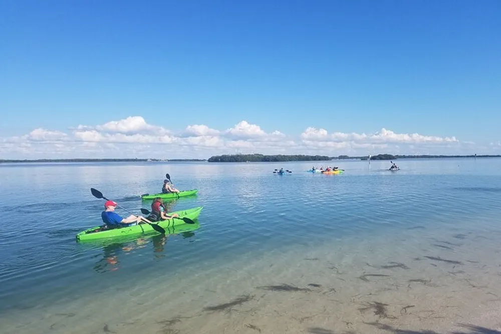 The image shows people in colorful kayaks enjoying a calm day on a clear tranquil body of water under a blue sky dotted with white clouds