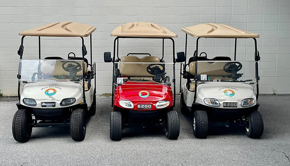 Three golf carts are parked side by side with the central one being red and the others white all featuring a logo on the front
