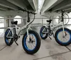 Two fat-tire electric bicycles are parked under a bridge near a body of water