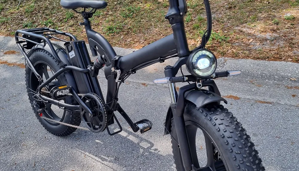 The image shows a black foldable electric bicycle with fat tires parked on a paved surface