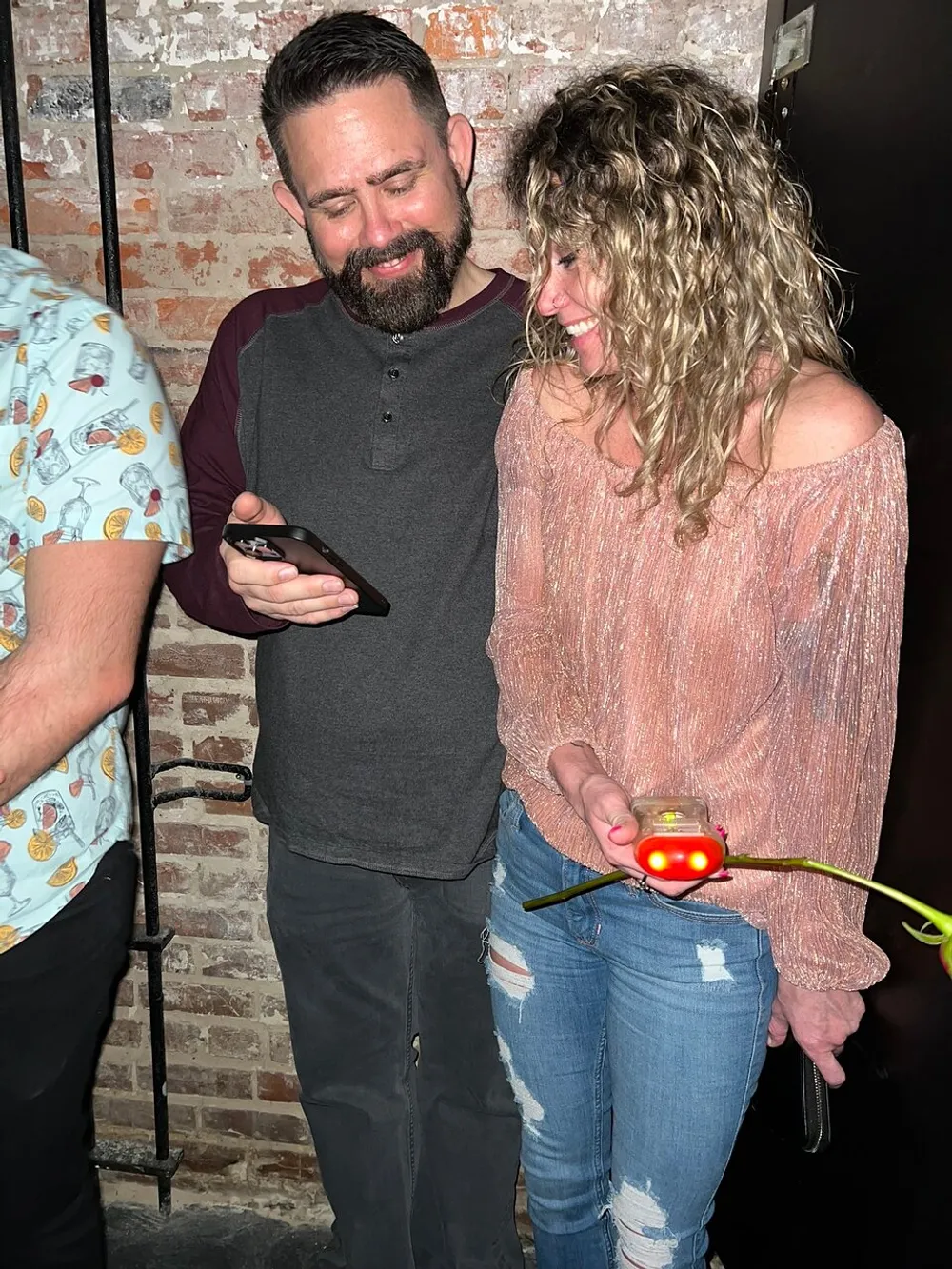 Two people share a moment of laughter while looking at a smartphone with the person on the right holding a toy with glowing red lights