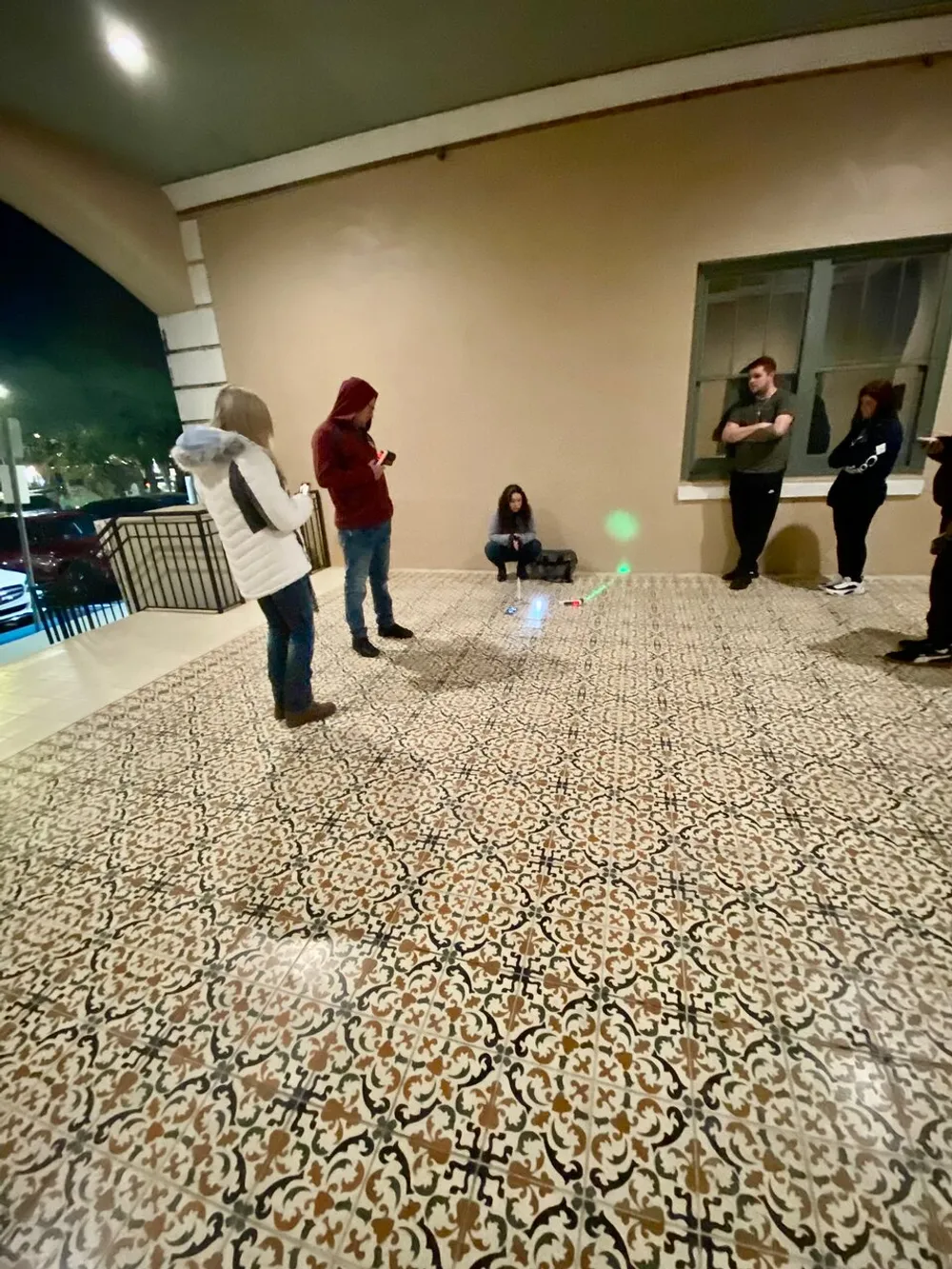 A group of individuals appears to be engaged in casual conversation or waiting for an event in an outdoor covered area with patterned flooring at night