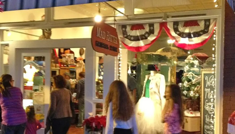 The image depicts a bustling evening scene outside a store named Mad Hatter with people walking by and festive decorations visible through the storefront