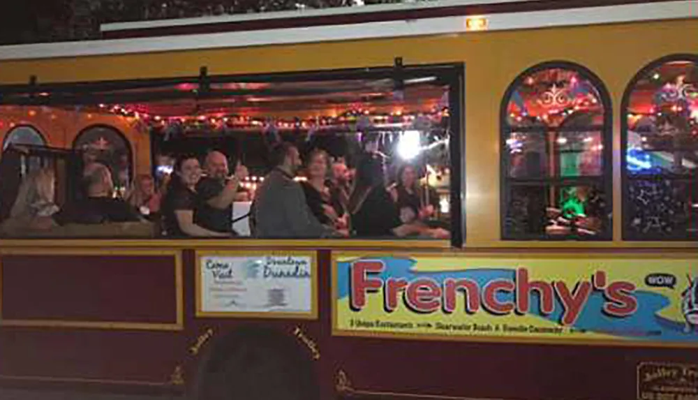 A group of people are enjoying themselves on a festive trolley-style party vehicle decorated with lights and advertisements for Frenchys