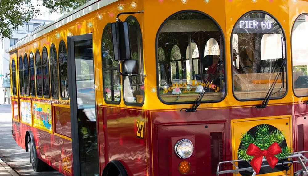 A yellow and red trolley with festive decorations is parked on a sunny street