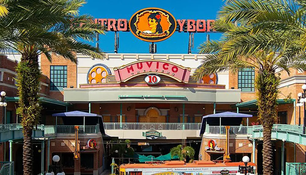 The image shows a colorful palm-lined movie theater entrance with a retro style and the name Muvico 10 displayed prominently above the doors