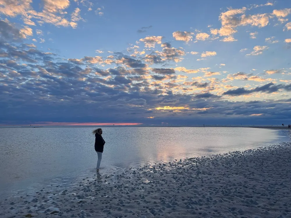 A person stands on a beach watching a beautiful sunset with scattered clouds painted by the fading light