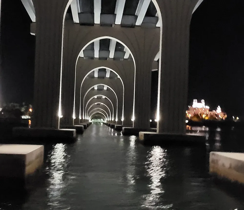 The image features a nighttime view of a series of illuminated arches under a bridge reflected in water creating a tunnel-like effect with lights visible in the background