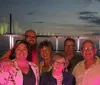 A group of passengers enjoys a sunset cruise near the coast on a pontoon boat with a tranquil ocean backdrop while an inset image shows a brightly lit bridge reflecting on the water at night