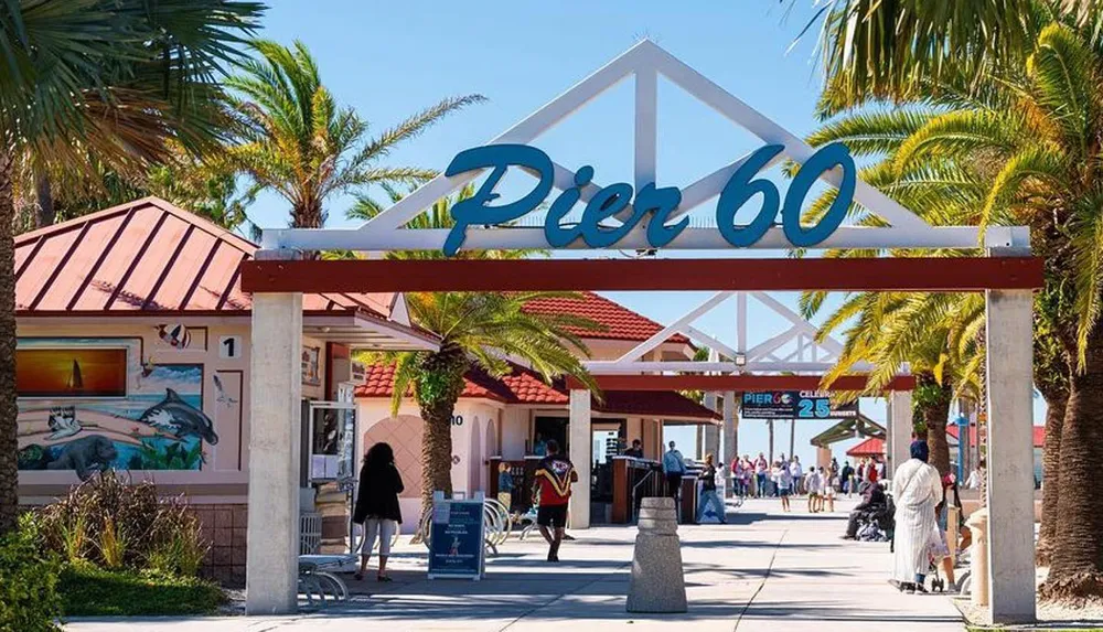 The image shows the entrance to Pier 60 marked by a large sign with people strolling around on a sunny day with palm trees lining the path