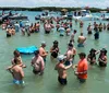 A group of people is enjoying a sunny day in the water near a boat named COASTAL CRUISES with some holding drinks and one woman cheerfully raising her arm in the air