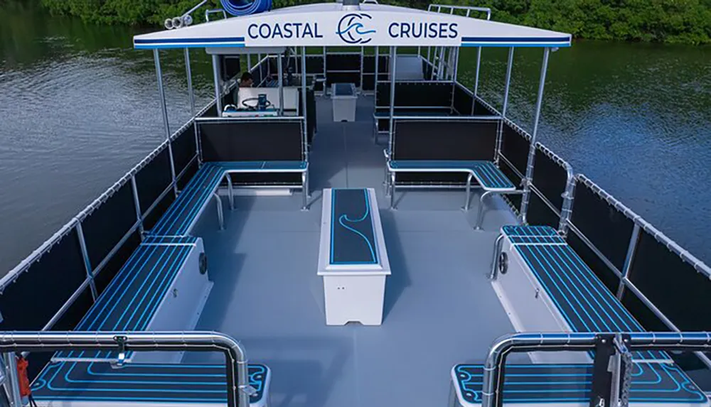 The image shows an empty double-decker party boat from an aerial perspective featuring neat rows of benches a steering station and the name COASTAL CRUISES printed on its canopy
