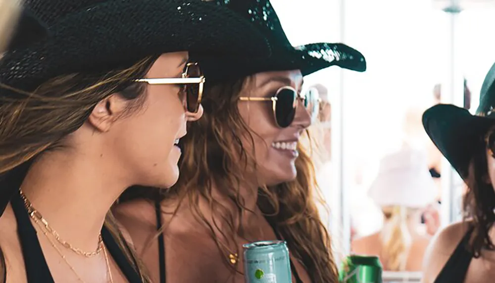 The image shows two smiling women wearing sunglasses and sunhats suggesting a sunny leisurely setting