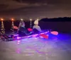 Two individuals are nighttime kayaking with colorful lights illuminating the water around their kayak