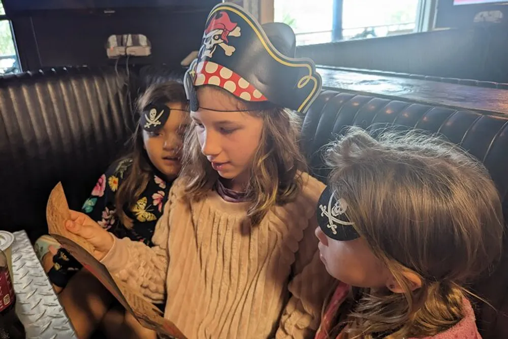 Three children two wearing pirate hats are looking intently at a menu in a restaurant booth