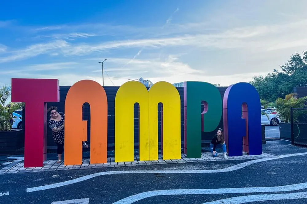 Two people are posing next to a large colorful sign that spells out Tampa