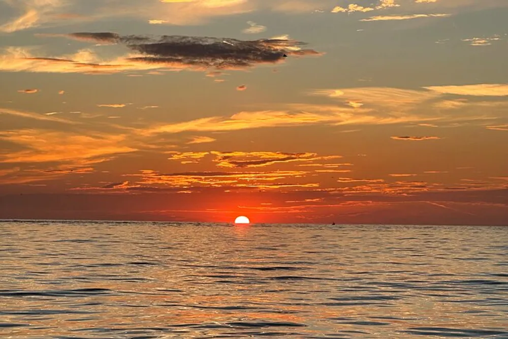 The image captures a serene sunset with a radiating orange sky and the sun dipping into the calm sea