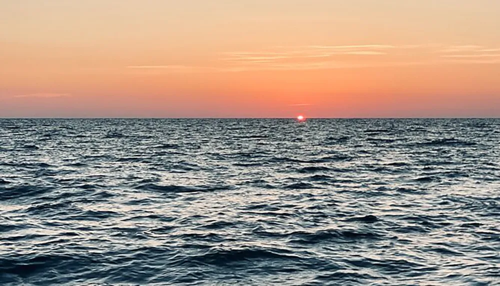 The image captures a tranquil sunset over a wavy sea with warm hues of orange and pink blending into the horizon