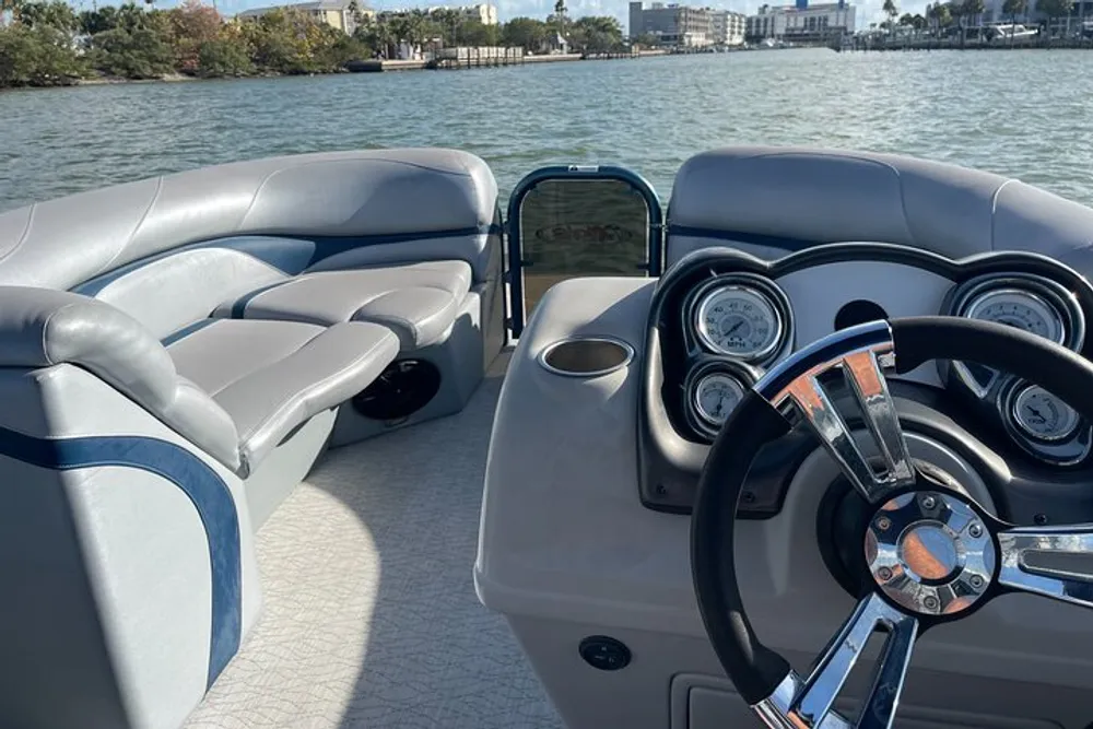 The image shows the helm and passenger seating of a modern boat with a view of the water and some distant shorefront
