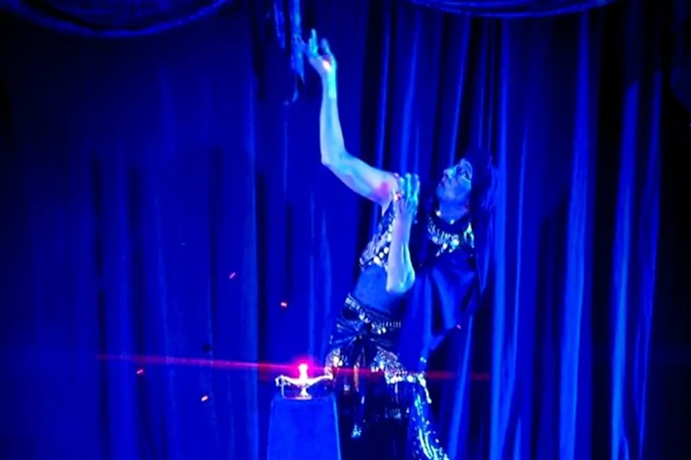 A performer is interacting with a red laser beam on stage amidst theatrical lighting and draped curtains