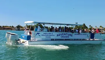 A group of people are enjoying a sunny day on a shelling and dolphin watch tour boat cruising through blue waters.
