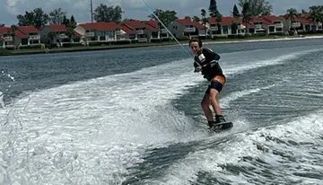 A person is wakeboarding on a body of water with houses in the background.