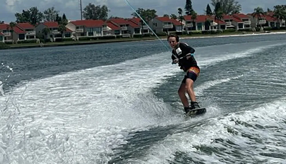 A person is wakeboarding on a body of water with houses in the background